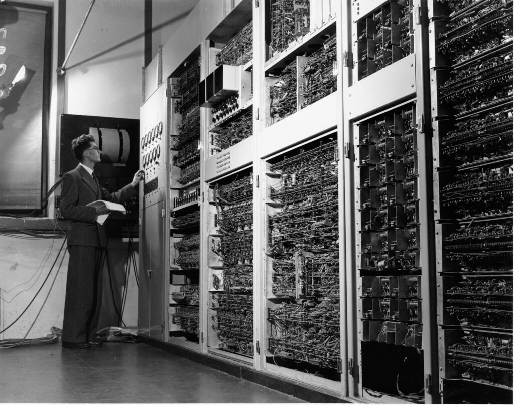 Black-and-white photo of large mainframe computer cabinets with an operator